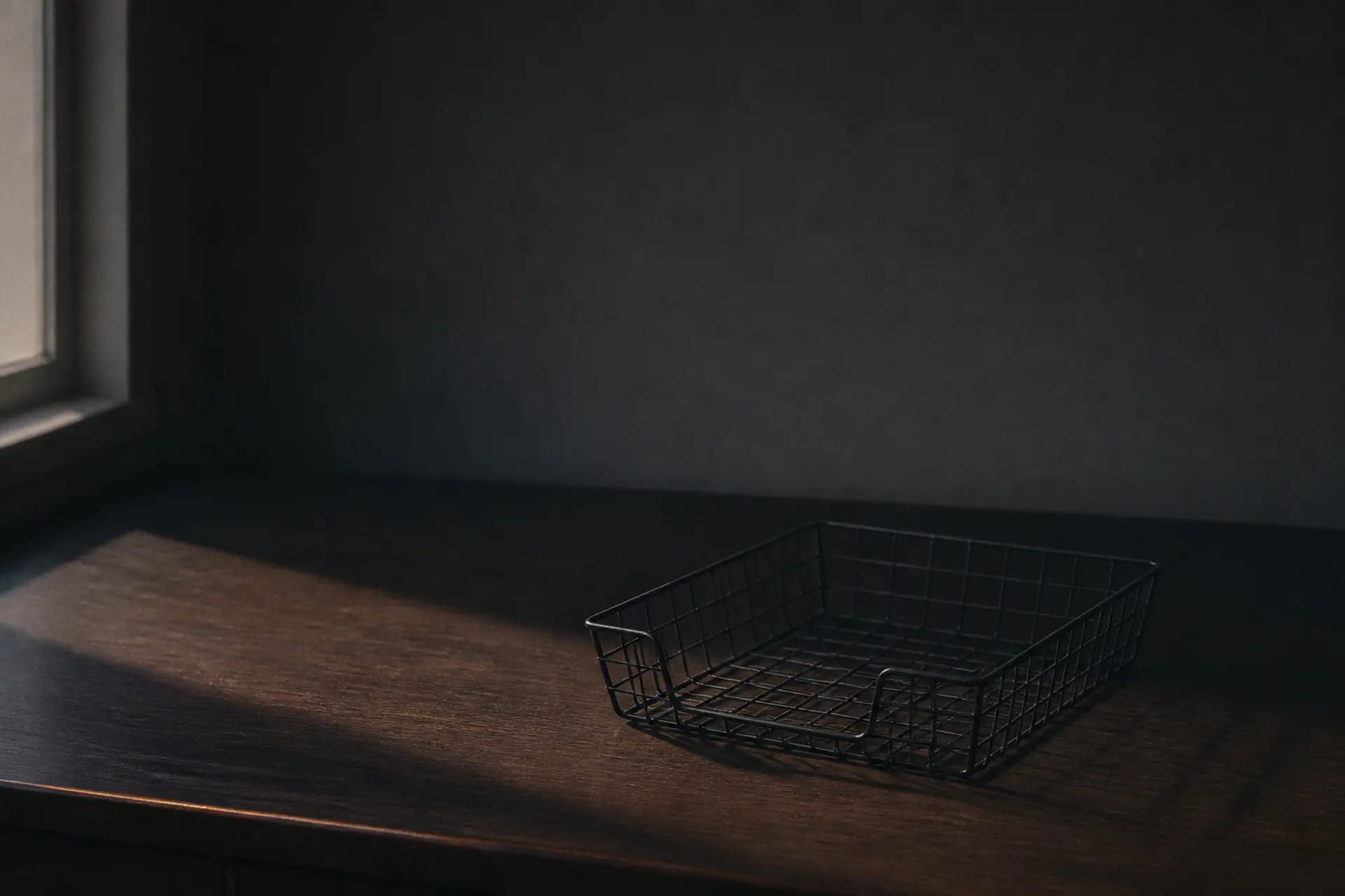 An empty wire mail tray on a bare desk, lit by morning light through a window